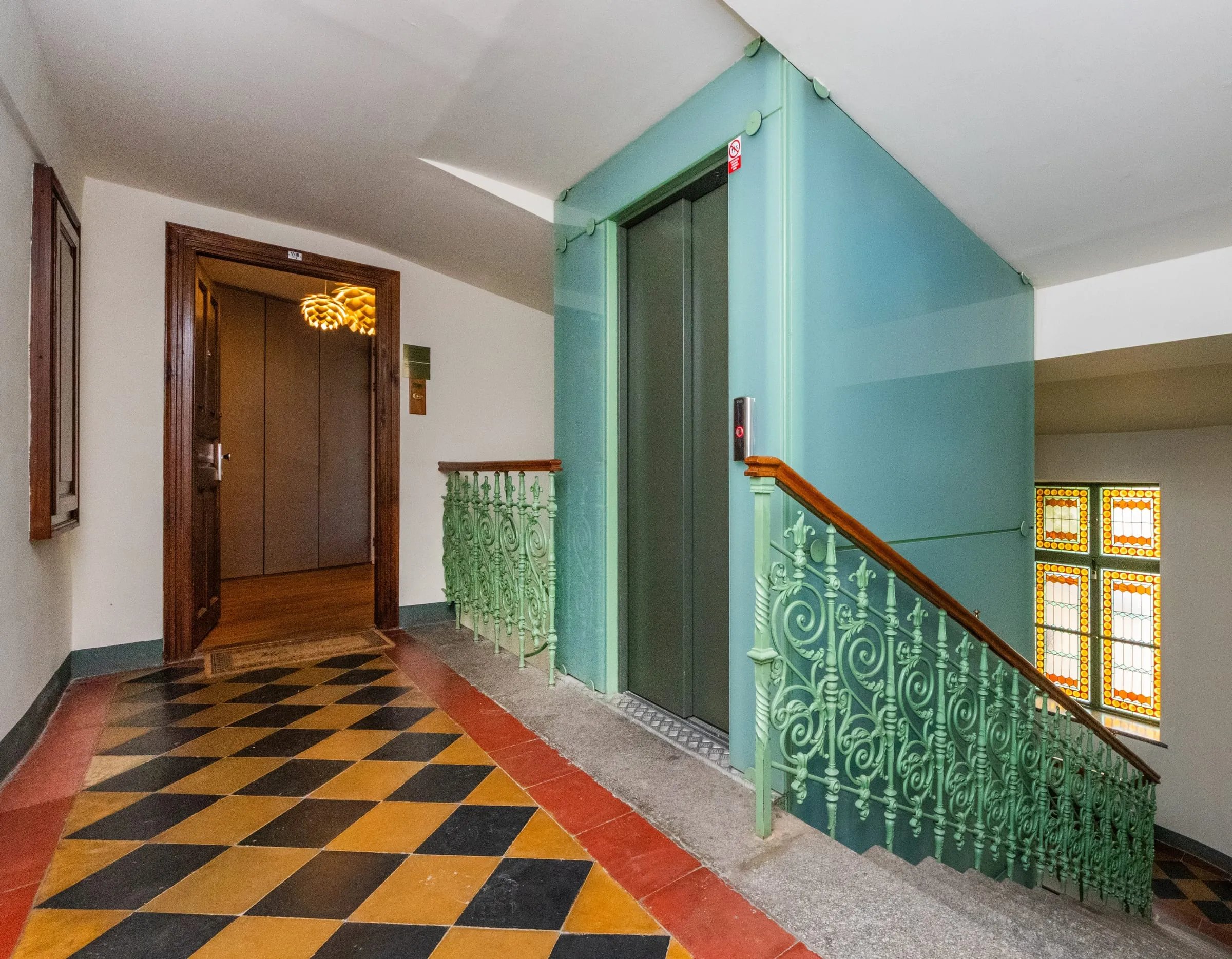 Art Nouveau stairwell with a green lift and patterned floor tiles