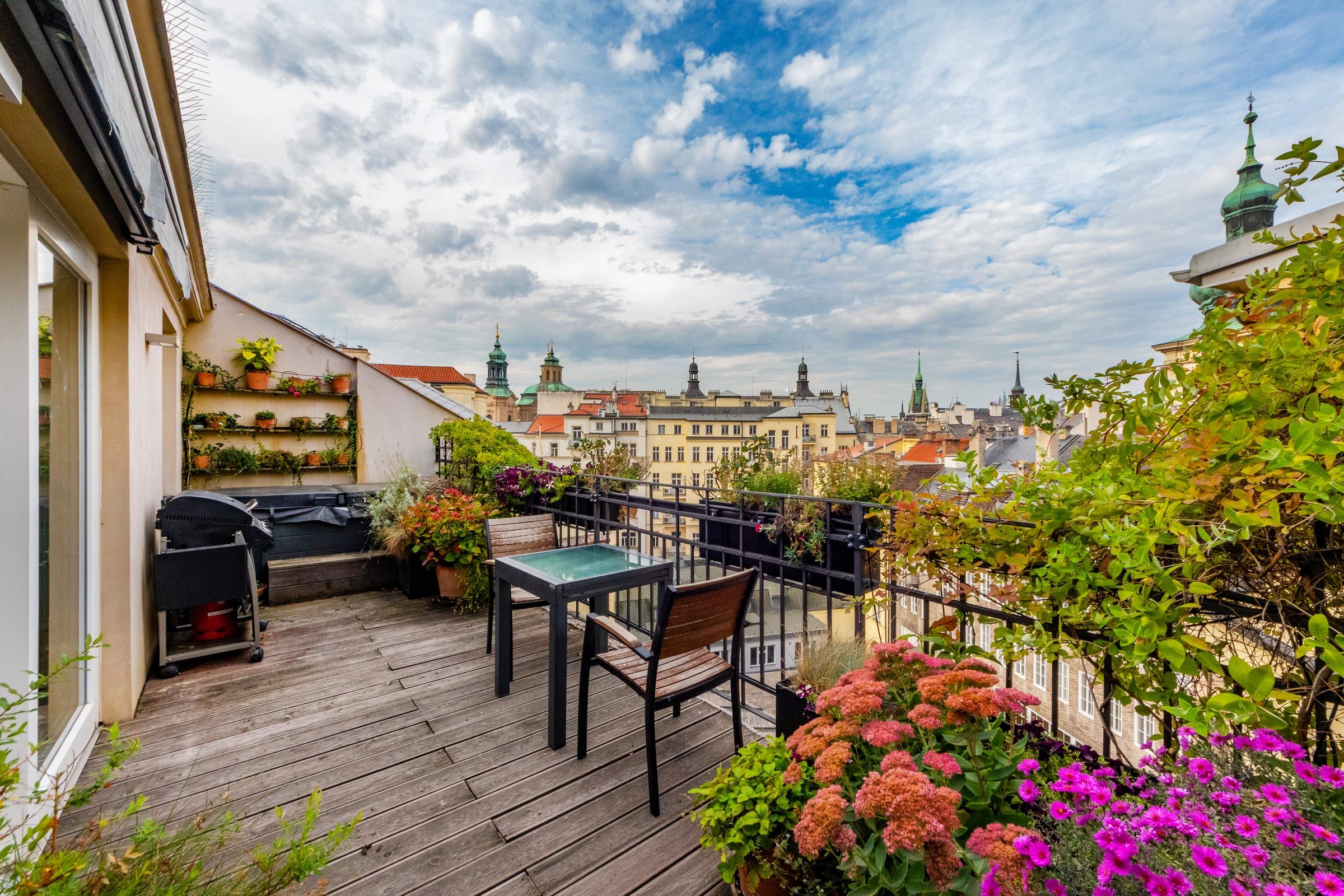 Wooden terrace full of flowers with a grill and an extendable table over the Old Town rooftops